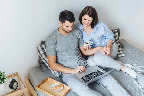 stock image Wife and husband make shopping online, choose present for their little child in internet, look at laptop computer, enjoy togetherness in bedroom, drink hot beverage. People, leisure, technology