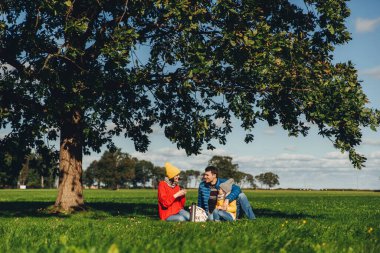 Yeşil çimenlerin üzerinde oturup, sıcak çay içmek, birbirleri ile iletişim, sakin atmosferi tadını çıkarın, mavi gökyüzü ve güzel manzaralar hayranım sonbahar piknik, mutlu bir aile var. Dostu aile üyeleri birlikte
