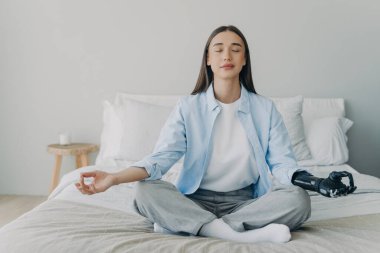 Engelli kadın yatakta nilüfer pozuyla meditasyon yapıyor. Sensörlü biyonik protezi olan beyaz bir kız. Gözler kapalı, miyoelektrik uzuv. Stres atma..