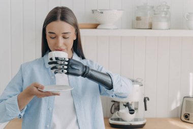 Özürlülerin rutini ve yaşam kalitesi. Siber elli güzel kız çay fincanı tutuyor, içiyor. Modern robot uzuvlarda yakalama sensörleri. Ev mutfağı sahnesi.