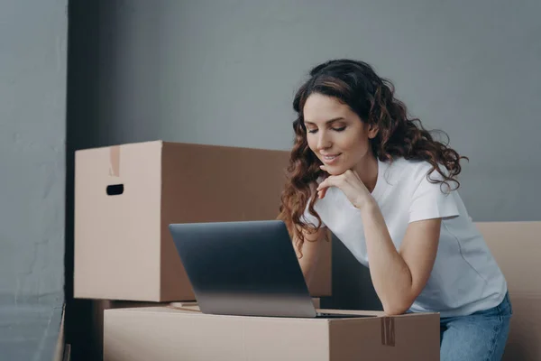 stock image Hispanic girl, delivery service worker, prepares online orders at laptop amidst cardboard boxes. Small business owner manages parcels for shipment. E-commerce operations.