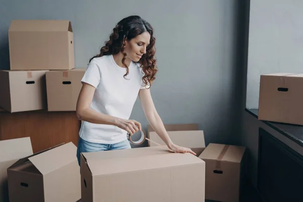Hispanic woman sealing cardboard box, preparing for moving day. Packing belongings, relocation and delivery service concept.