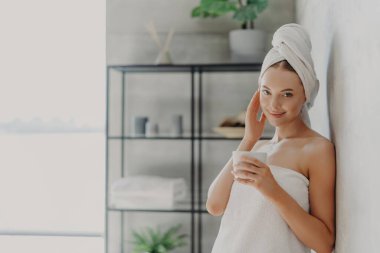 Memnun bir kadın, parlak tenli, havluya sarılı, rahat bir banyoda çay içen bir spa 'dan hoşlanıyor. Güzellik ve rahatlama.