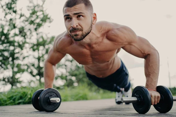 筋肉の男は プッシュアップを行い 屋外に焦点を当て バーベルで腹筋を訓練します スポーティライフスタイル — ストック写真