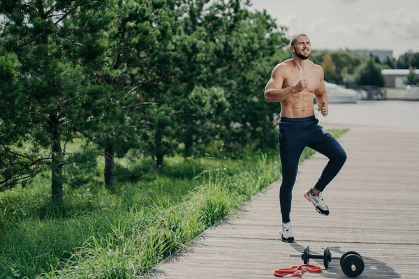 アクティブな男は屋外にジャンプ ジョギングのために暖まる スポーツパンツやスニーカーを身に着けています 裸の胴と演習 — ストック写真
