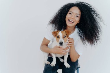 Yeni Jack Russell Terrier 'ı olan neşeli kıvırcık kız, gülümsüyor, oynuyor ve sevişiyor. Mutlu anlar izole edilmiş portrede..