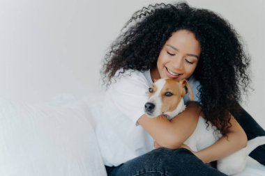 Gündelik giysiler içindeki Afrikalı Amerikalı kadın köpeğine sevgisini ifade ediyor. Sabahları rahat bir yatakta sarılıp yatıyorlar. Sahibi Jack Russell Terrier..