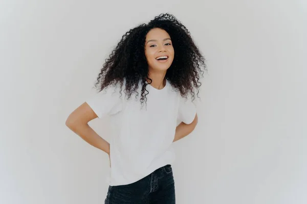 stock image Cheerful African American woman in casual clothes, laughing with hands behind back, isolated on white background.