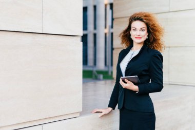 Resmî kadın, iş için gerekli tableti tutuyor. Güzel, kıvırcık saçlı kadın, çekici görünüşlü, işe gidiyor..