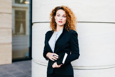 Ofisteki çalışkan kadın işçi, elinde kalem, ayakta duruyor, odaklanmış..