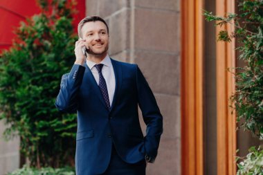 Girişimcinin telefonda konuşmasına, resmi siyah takım elbise giymesine, dışarıda durmasına sevindim. Kafe / restoran yakınlarında iş ortağı bekliyor..