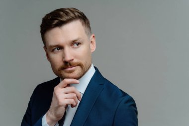 Sakallı işadamı, karar verir, resmi giyinir, geleceği düşünür. Gri arkaplan, metin için boşluk.