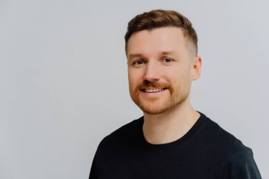 Sevinçli kızıl adam, yakın plan, pozitif ifade. Siyah tişört, gri duvar. Hayattan zevk almak, olumlu duygular..