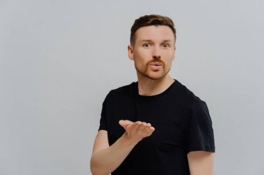 Tıraşsız yakışıklı bir adam kız arkadaşına hava öpücüğü veriyor. Aşkı ve flörtü ifade etmek. Gri stüdyo arka planında izole edilmiş..