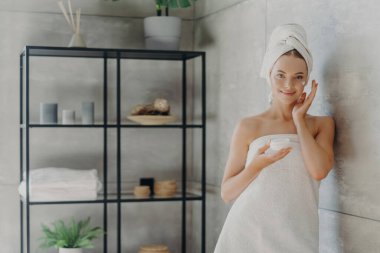 Sağlıklı model krem kullanır, kozmetik kavanozu tutar, havluya sarılır, sıcak banyo duvarının yanında. Cilt bakımı
