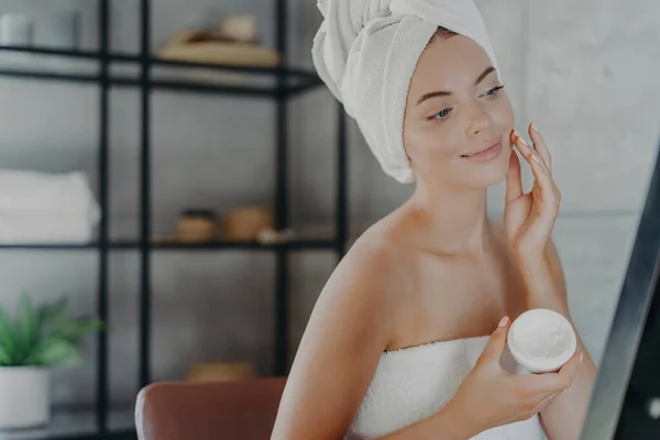女性は健康的な肌のためのシャワー後の顔のクリーム 賞賛の反射 タオルラップ アンチエイジングを適用してください スキンケアコンセプト — ストック写真