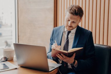 Resmi giysiler içinde konsantre girişimci notlar alır, dikkatle dinler, kafede dizüstü bilgisayarında kulaklıkla webinar izler..