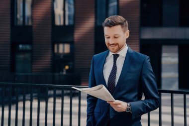 Başarılı genç bir şirket sahibi, gülümsüyor, tatmin edici bir şekilde gazete okuyor, ofis binasının önünde el ele duruyor..