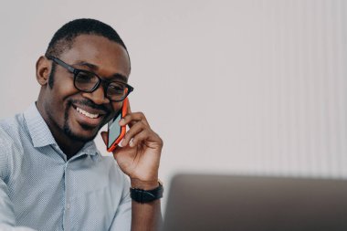 Dost canlısı Afrikalı Amerikalı iş adamı, gülümsüyor, iş telefonlarına cevap veriyor, laptop ekranına bakıyor, danışman müşteriye bakıyor, mobil sohbetten keyif alıyor..