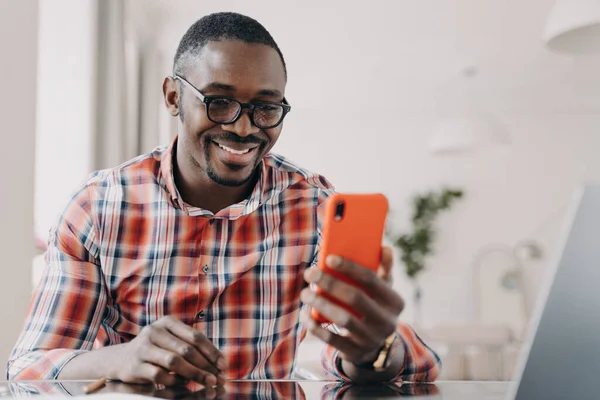 Улыбающийся Афроамериканец Использующий Мобильные Приложения Держащий Смартфон Сидящий Столом Счастливый — стоковое фото