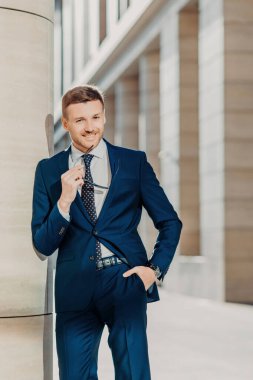 Düşünceli neşeli sakallı erkek girişimci hoş gülümseme vardır, siyah takım elbise giyiyor, güneş gözlüğü, pozlar kapalı, Toplantı ve ortağı ile sözleşme imzalama başarılı iş memnun tutar