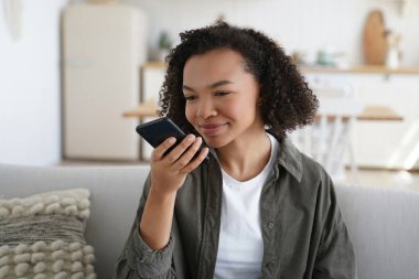 Melez bir genç kız internette sohbet ediyor, telefonuna sesli mesaj bırakıyor. Gülümseyen, sanal asistan kullanan ya da evdeki kanepede çeviri uygulaması kullanan.