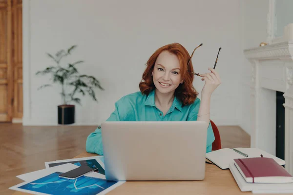 Glad Rödhårig Kvinna Coworking Utrymme Fungerar Laptop Håller Glasögon Bläddrar Stockbild