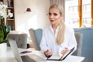 portrait of young adult attractive blonde businesswoman in white shirt working in home office