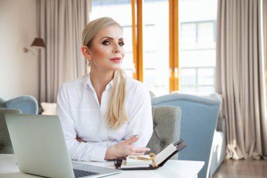 portrait of young adult attractive blonde businesswoman in white shirt working in home office
