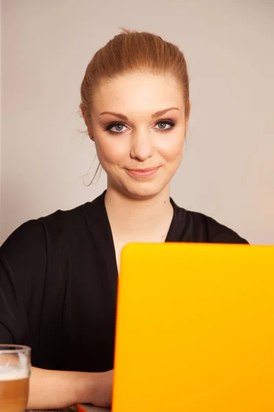 穿着漂白衬衫在电脑上工作的漂亮的金发女学生 图库图片