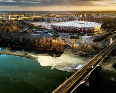 Vistula Nehri ve Poniatowski Köprüsü ile şafak vakti Varşova 'daki Ulusal Stadyum' un hava manzarası. Yumuşak sabah ışığı etrafındaki şehir manzarasına karşı modern tasarımı vurguluyor.. 
