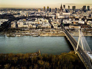 Şafak vakti Vistula Nehri 'ni geçen Witokrzyski Köprüsü ile Warsaw' ların gökyüzü manzarası. Modern şehir manzarası nehir ve yeşil alanlarla çelişiyor ve sabahın erken saatlerinde sakin bir manzara yaratıyor..