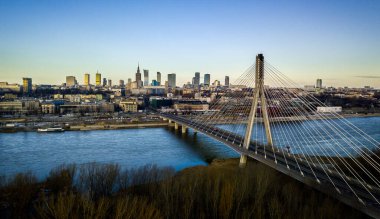 Şafak vakti Vistula Nehri 'ni geçen Witokrzyski Köprüsü ile Warsaw' ların gökyüzü manzarası. Modern şehir manzarası nehir ve yeşil alanlarla çelişiyor ve sabahın erken saatlerinde sakin bir manzara yaratıyor..