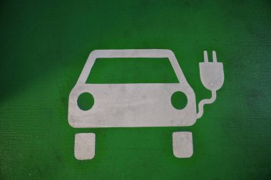 Yan tarafında fiş olan bir araba. Araba elektrikli ve şarj oluyor. Görüntü yeşil ve beyaz