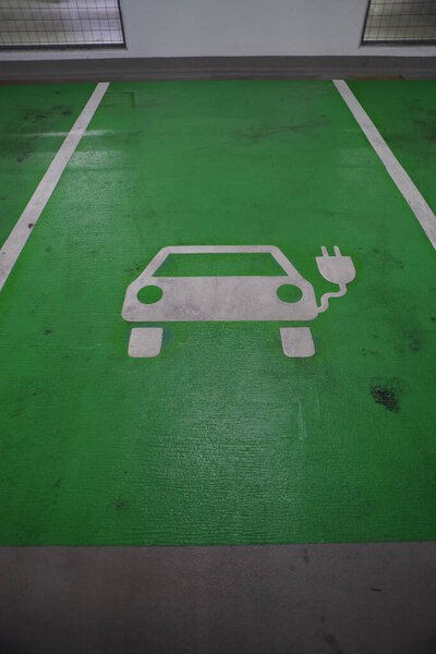 Парковка с зеленым парковочным местом с надписью "EV Зарядка". Парковочное место обозначено белым символом автомобиля