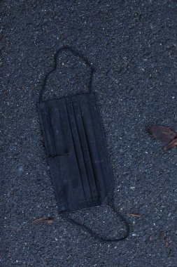 Yerde siyah bir yüz maskesi var. Maske kirli ve içinde bir delik var. Sahne karanlık ve kasvetli, görüntüdeki tek parlak nesne maske.