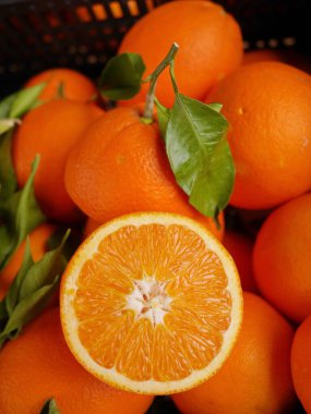 A basket of oranges with one orange cut in half. The oranges are ripe and ready to eat. clipart