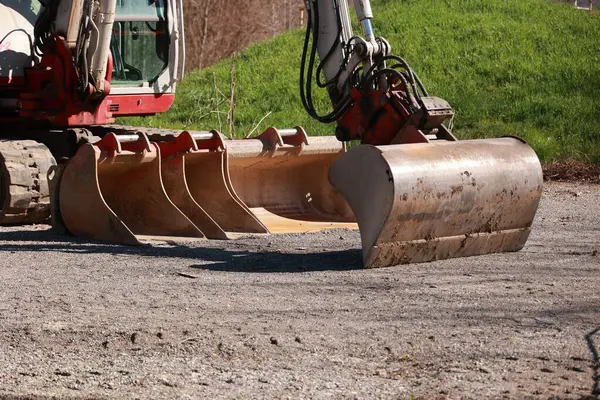 Kırmızı ve beyaz renkli büyük bir ekipman toprak bir yolda duruyor. Makine bir kepçe doldurucu, ve yolun ortasına yerleştirilmiş.