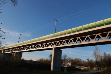 Yeşil korkuluklu ve içinden tren geçen bir köprü. Gökyüzü açık ve güneş parlıyor.