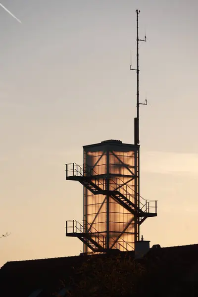 Kenarında merdiven olan yüksek bir kule. Kule aydınlandı ve gökyüzü turuncu