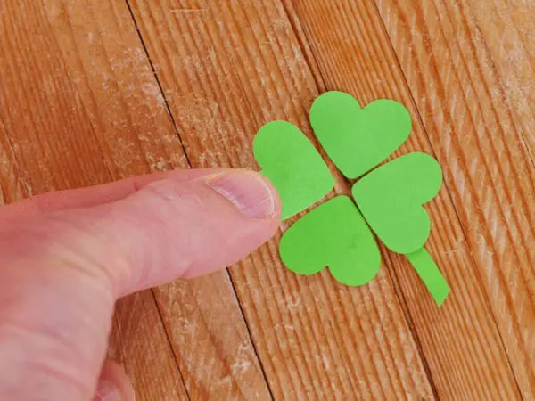 Bir el, dört yapraklı yoncanın parçası olan yeşil kağıt bir kalbe dokunuyor. Özen kavramı ve detaylara dikkat, kişinin kalbi dikkatle incelediği gibi..