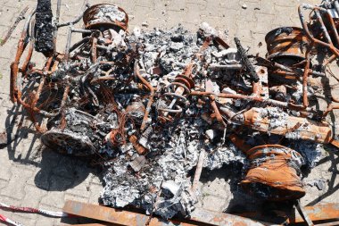 Bir araba yanıyor ve tahrip edildi. Araba kül ve enkaz yığınıyla çevrili.