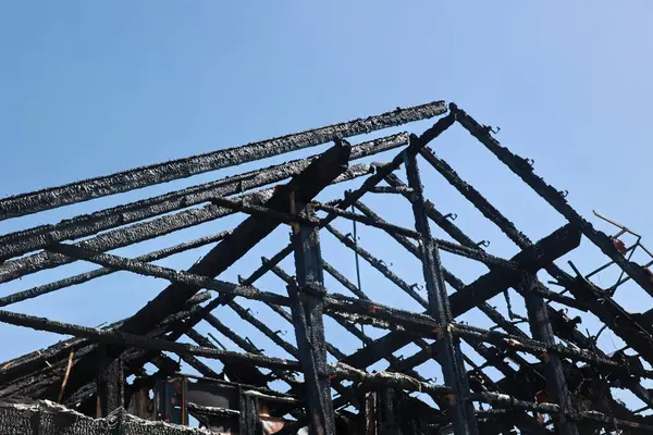 Siyah çatılı ve arkasında mavi gökyüzü olan bir bina. Çatı yandı ve bina harabeye döndü.