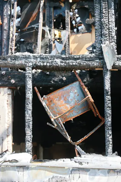 Bir sandalye baş aşağı ve alevler içinde, bacakları ve koltuğu kömürleşmiş ve kararmış. Yangın, kömürleşmiş ve yanmış bir dağınıklık bırakarak çevreye yayıldı. Sahne kaotik ve tehlikeli.