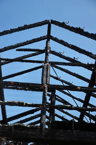 Arka planda mavi gökyüzü olan siyah ve kömürleşmiş bir çatı. Çatı yanmış ve yanmış, görüntüye yıkım ve yıkım hissi veriyor.