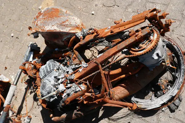 Yerde siyah zincirli ve siyah koltuklu bir motosiklet var. Motosiklet paslanmış ve yanmış.