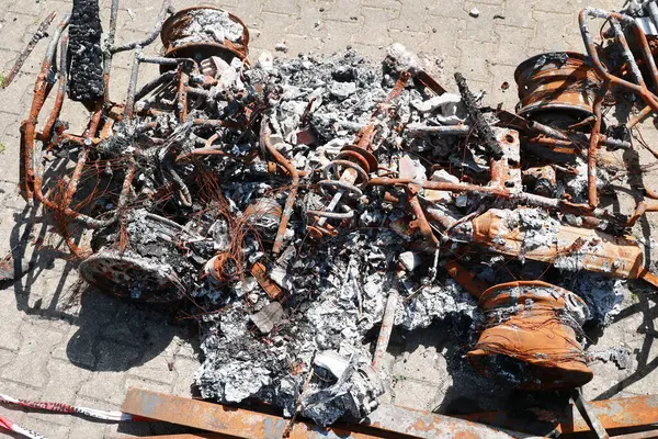 Bir araba yanıyor ve tahrip edildi. Araba kül ve enkaz yığınıyla çevrili.