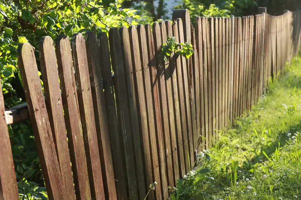 Kırık bölmeli ahşap bir çit. Çit çim ve yapraklarla çevrili.
