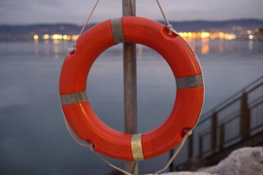 Kırmızı can yeleği metal bir direğe asılı. Su sakin ve gökyüzü karanlık.