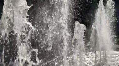Bir dizi çeşme havaya su püskürtüyor. Su beyaz ve fıskiyeler bir parkta.